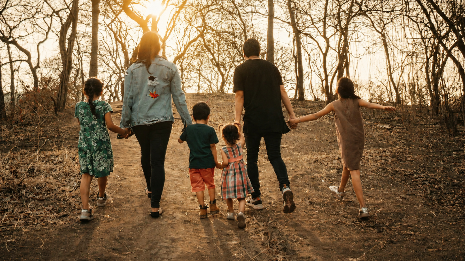 A family of six walking hand-in-hand along a wooded path toward the light